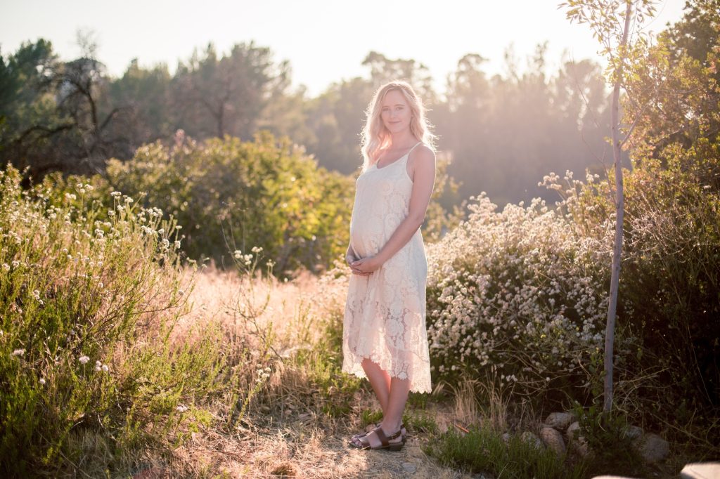 Young pregnant woman standing in a natural setting holding her baby belly
